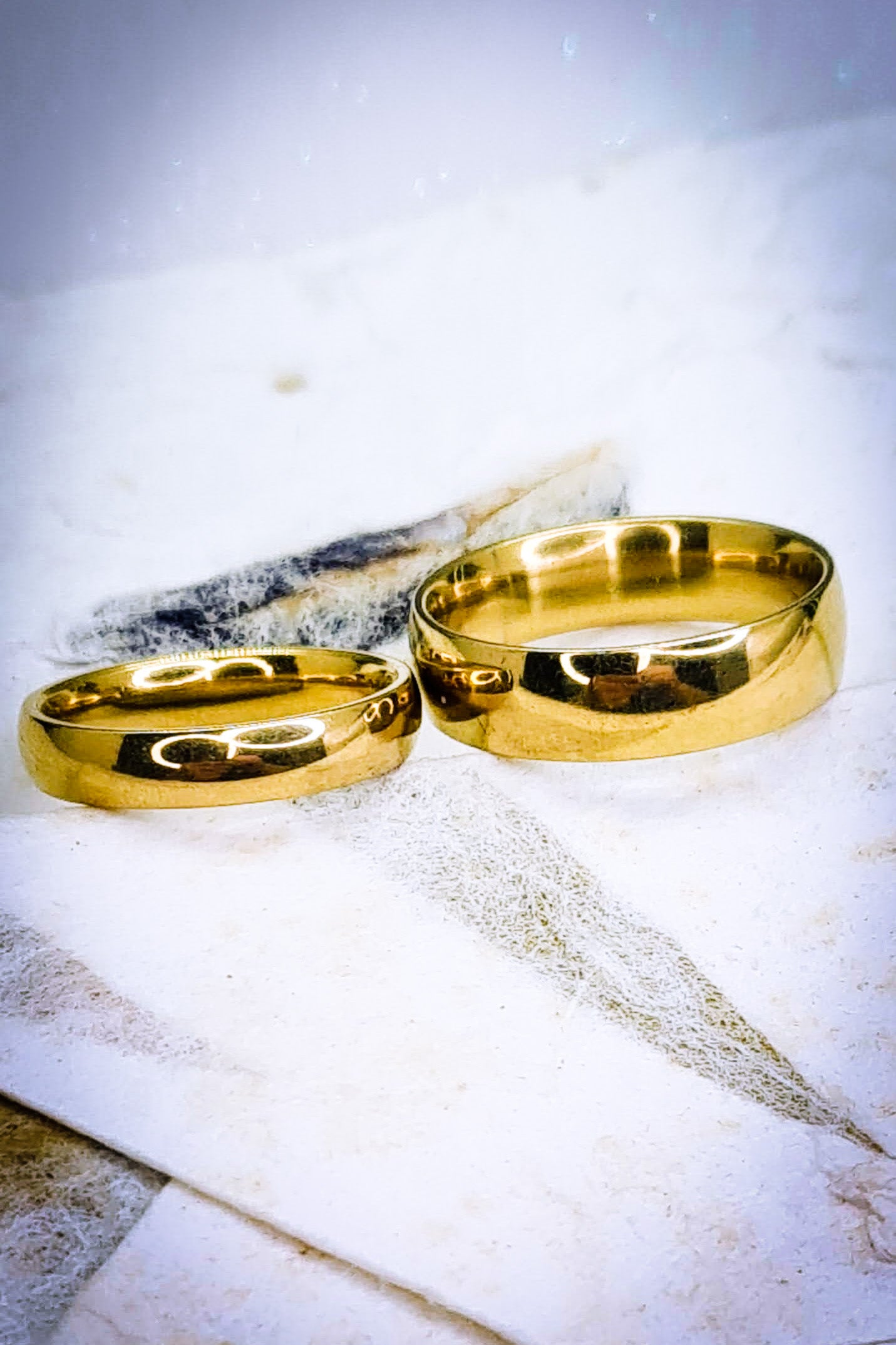 Anillos tipo alianza de matrimonio o pareja en acero inoxidable dorado y ancho de 4mm y 6mm. Se incluye grabado de nombres y fecha importante gratis. Posan sobre bolsa de cartón colores pastel.