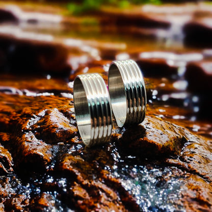 Dos Anillos tipo alianza de matrimonio o pareja en acero inoxidable bicolor y ancho de 6mm. Se incluye grabado de nombres y fecha importante gratis. Posan sobre riachuelo.