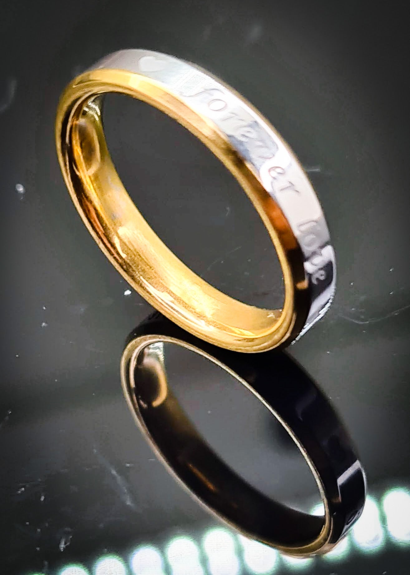 Anillo "Forever Love" tipo alianza de matrimonio o pareja en acero inoxidable bicolor y ancho de 4mm. Se incluye grabado de nombres y fecha importante gratis. Posa sobre fondo negro.