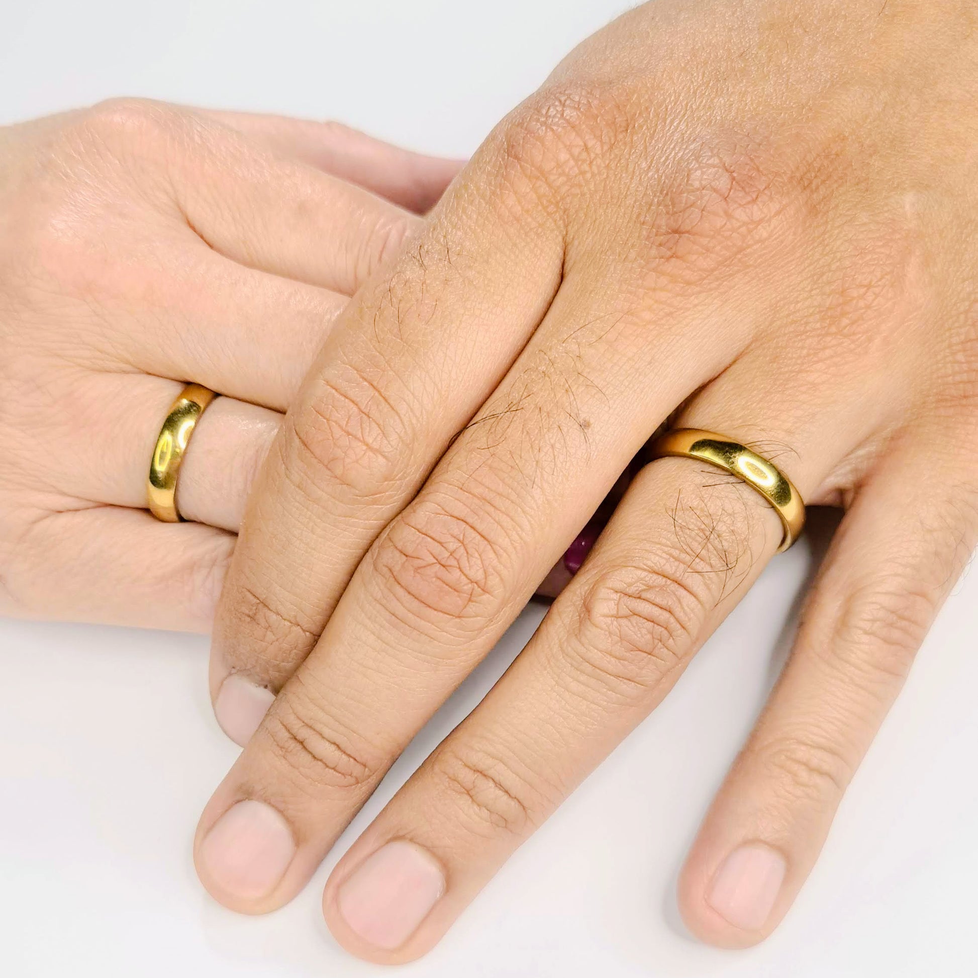Anillo Alianza en acero inoxidable dorado para parejas y novios, expuestos sobre la mano de una pareja. Grabado interior gratis.