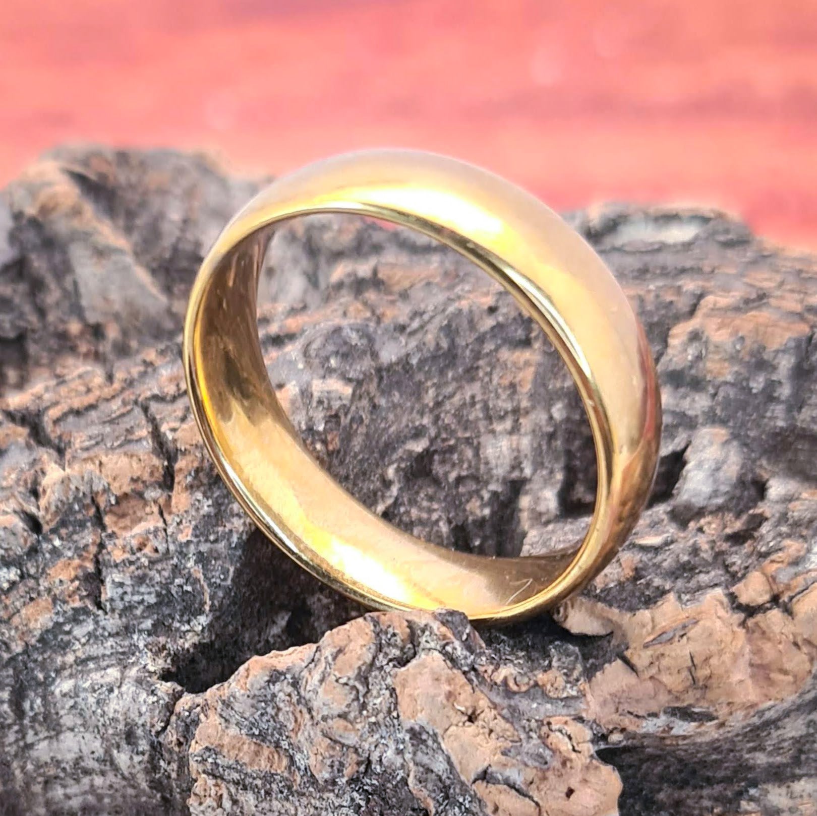 Anillo tipo alianza de matrimonio o pareja en acero inoxidable en color dorado y ancho de 6mm. El anillo está sobre un tronco. Se incluye grabado de nombres y fecha importante gratis.