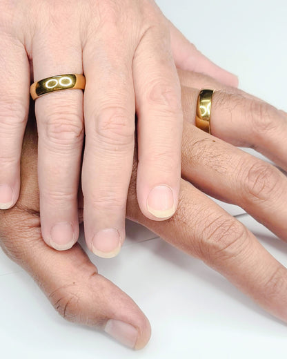 Anillo tipo alianza de matrimonio o pareja en acero inoxidable en color dorado y ancho de 6mm. Se muestra el anillo en puestos en las manos de una pareja. Se incluye grabado de nombres y fecha importante gratis.